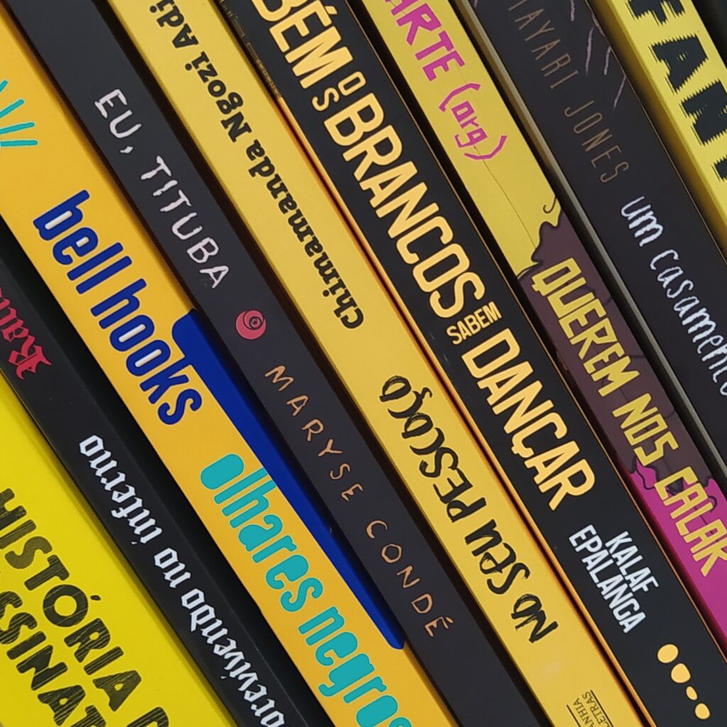Pilha com vários livros escritos por pessoas negras. Eles possuem lombadas amarelas e pretas, e estão organizados de uma forma em que as cores vão se alternando.